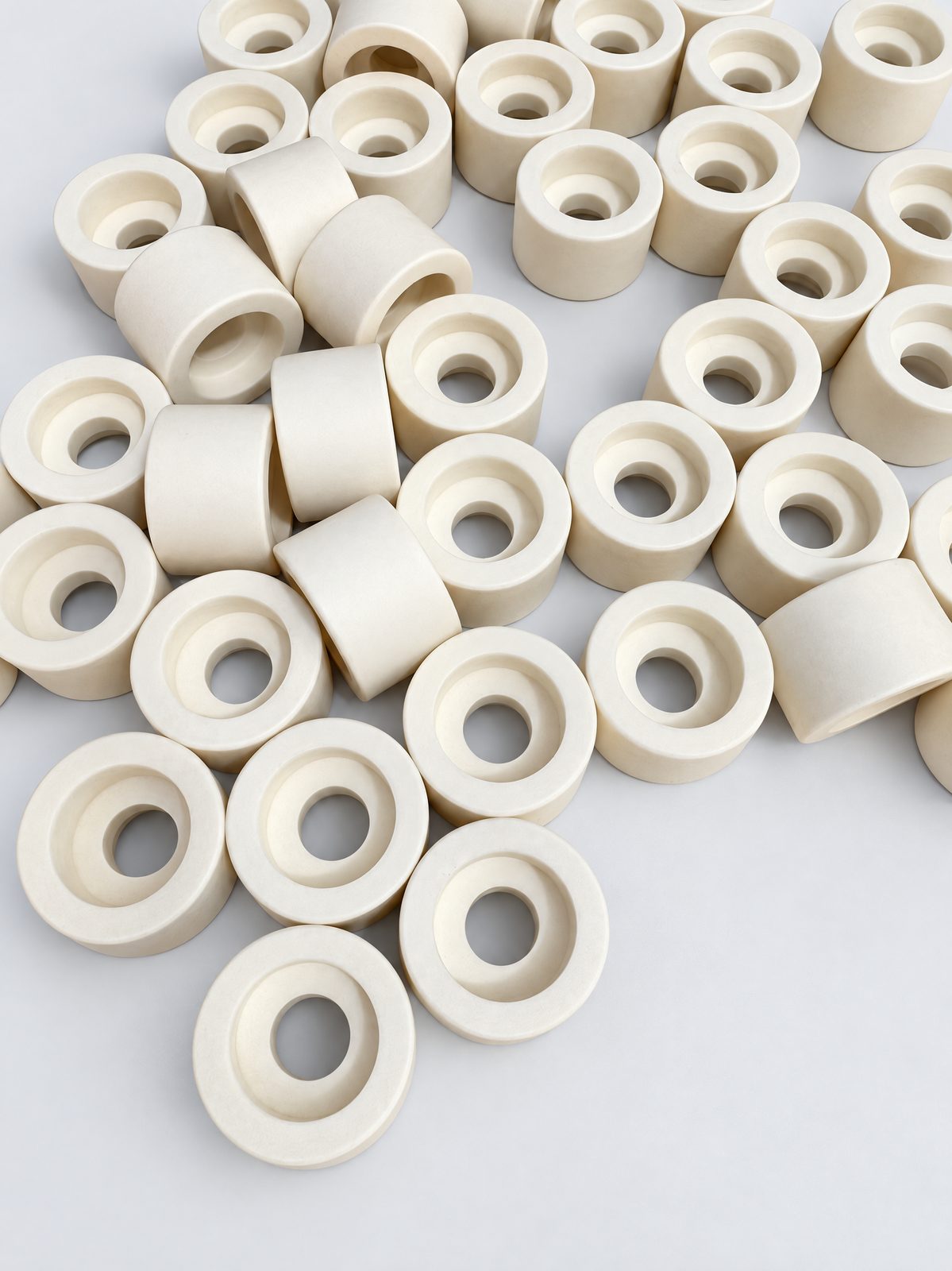 About forty short, thick ceramic rings with stepped bores scattered on a wooden table.