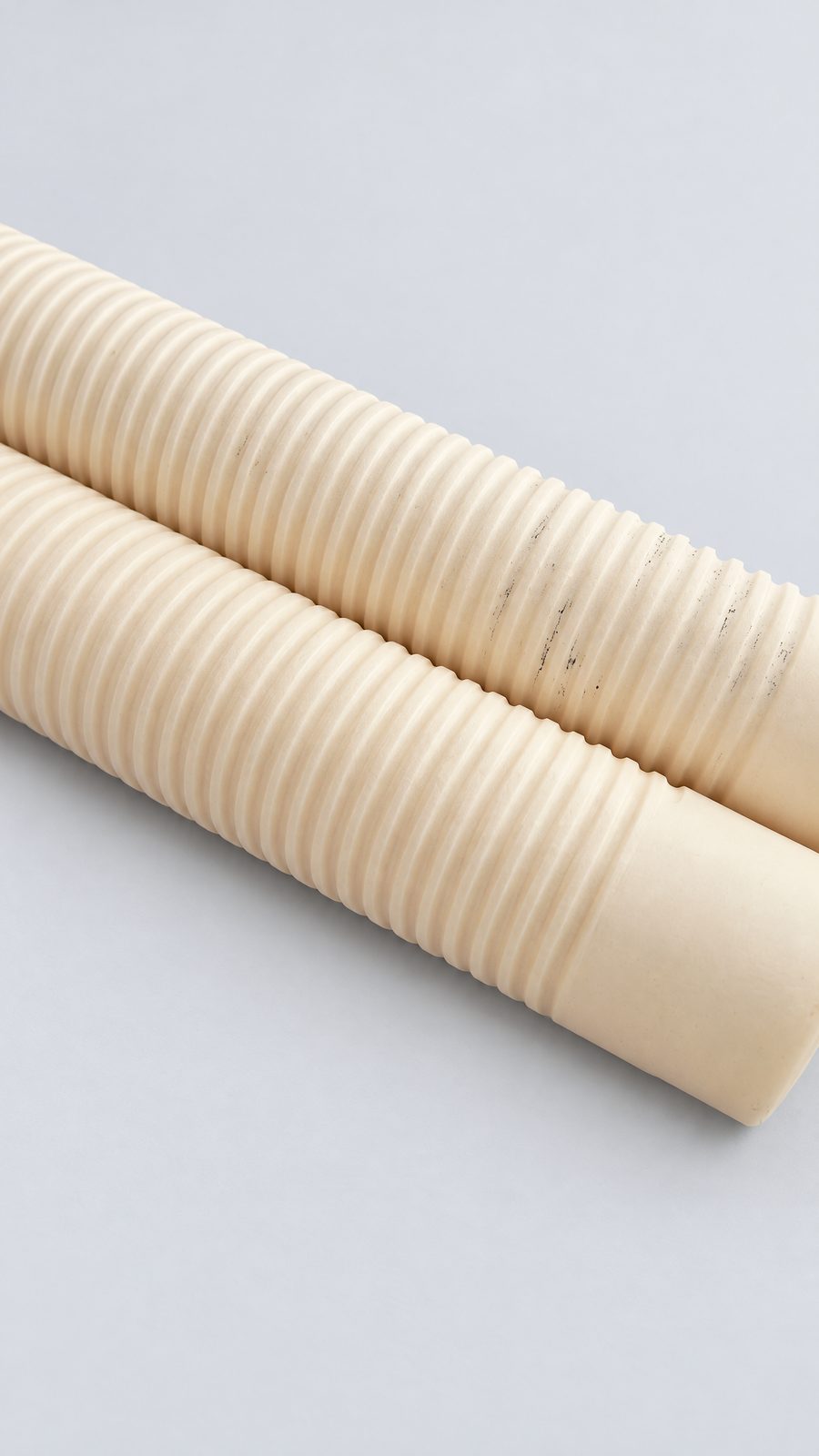 Two cream ceramic tubes on a black surface, each with a continuous helical groove along most of its length and a plain section at one end.