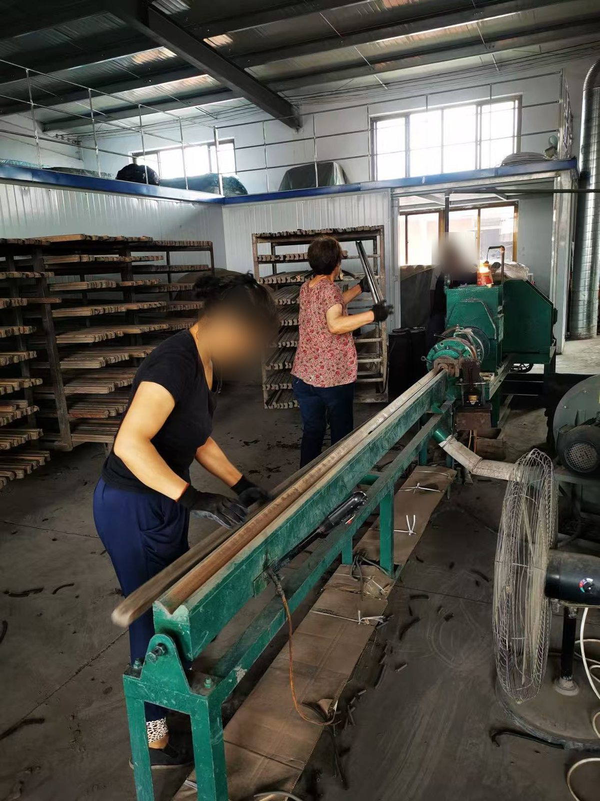Two workers at a green horizontal extrusion machine on the forming line.