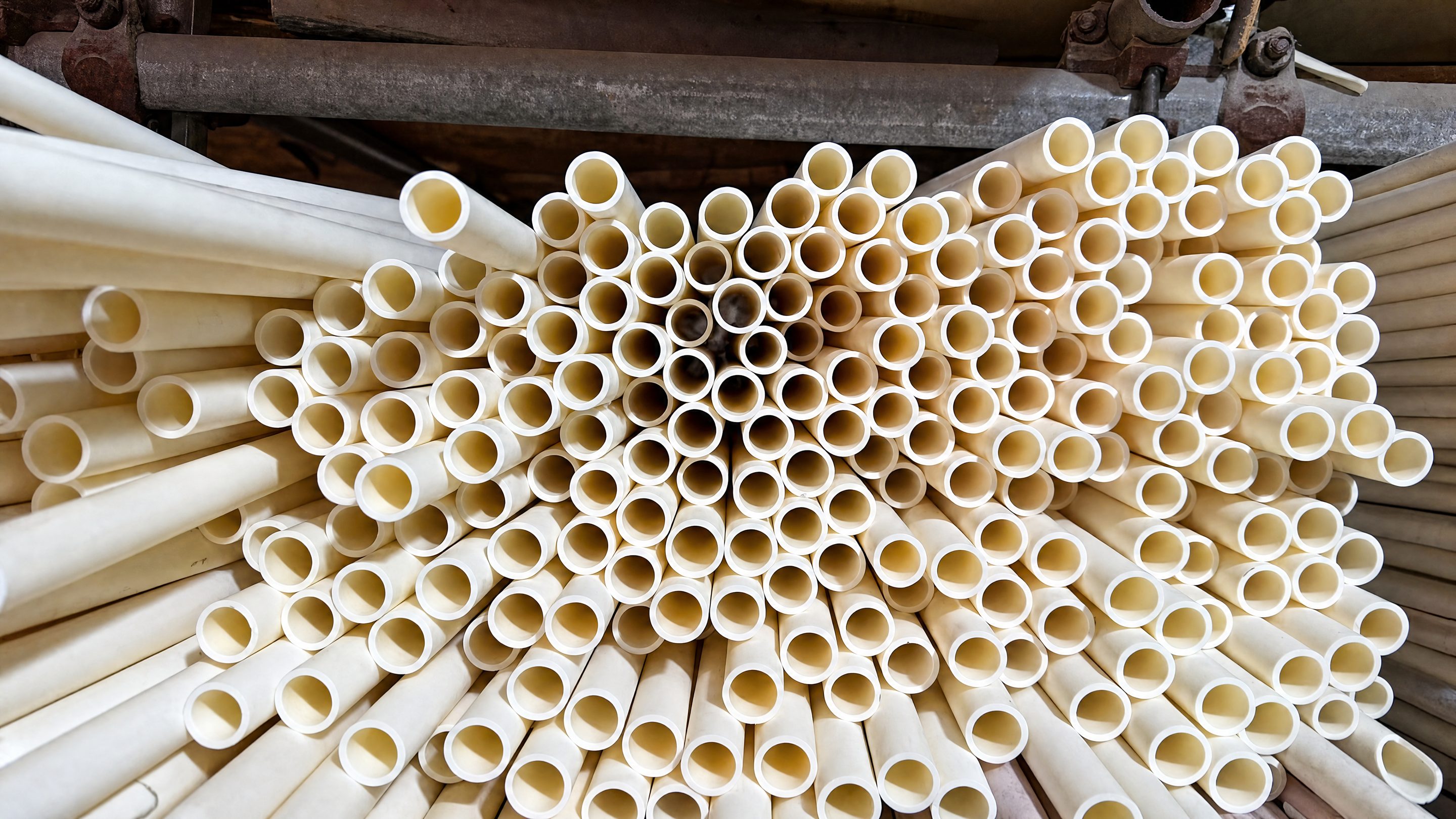End-on view of several hundred open-ended cream tubes in at least two diameters, lying on a rack of steel scaffold tubes.