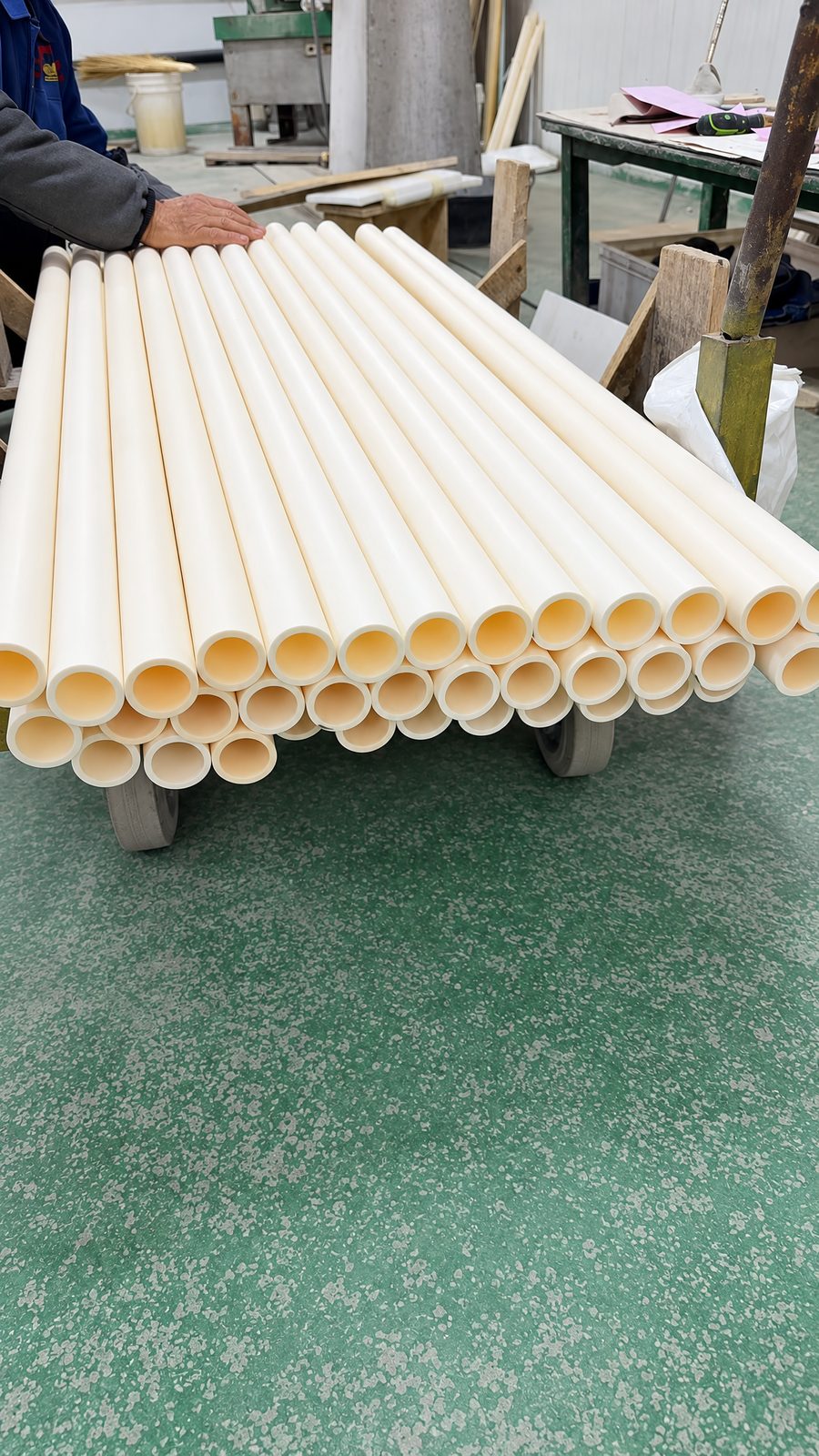About thirty long, large-diameter open-ended ivory tubes stacked in three layers on a low wheeled trolley in the workshop.