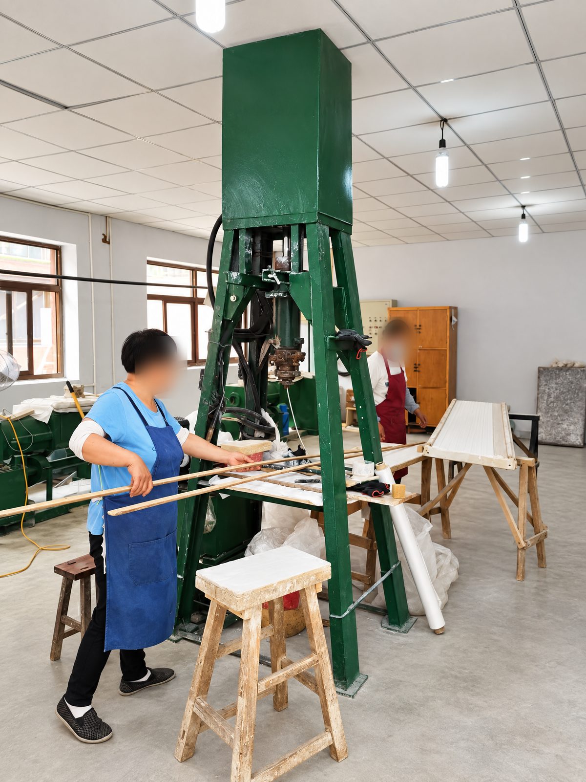An operator beside a tall green vertical hydraulic press used to form ceramic parts.