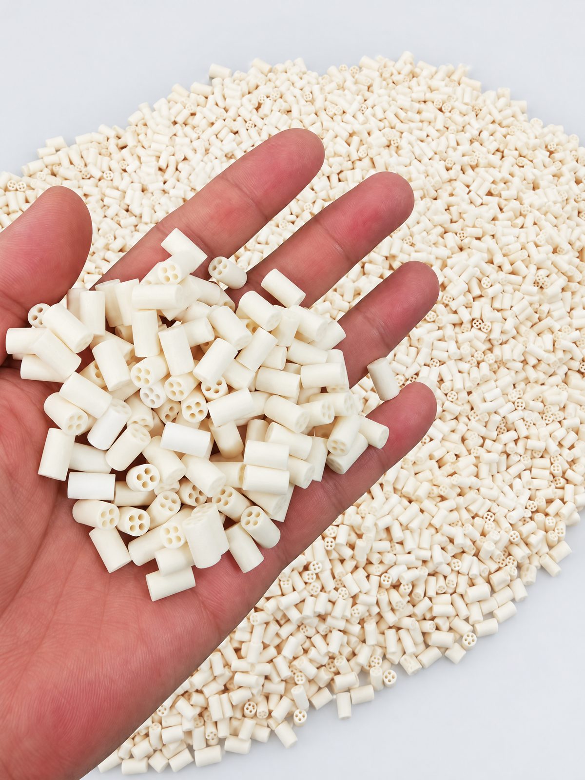 A palmful of short cream four-bore insulator beads held over a blue crate filled with the same beads.