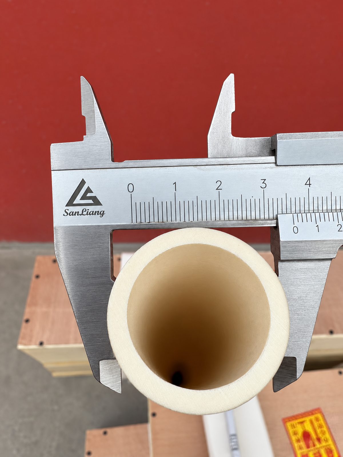 A steel vernier caliper with its jaws across the outside diameter of a thick-walled cream ceramic tube, seen end-on.