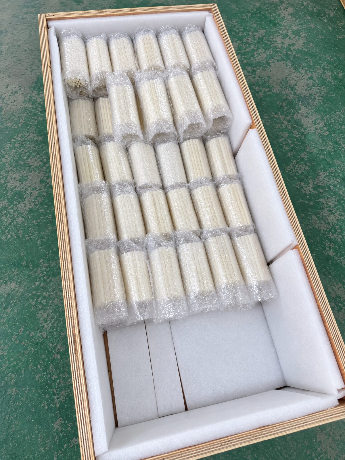 An open plywood crate lined with white foam on all sides, holding rows of bubble-wrapped bundles of short ivory tubes.